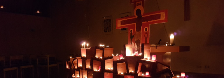In einer dunklen Kirche steht ein Aufbau aus Tonröhren und viel warmem Licht aus vielen brennenden Kerzen.