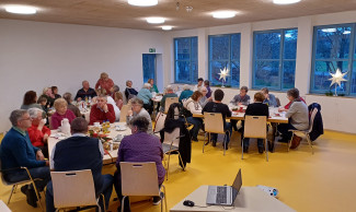 Im Mehrzweckraum des Kindergartens Flohkiste sitzen zahlreiche ältere Menschen an adventlich gedeckten Tischen.